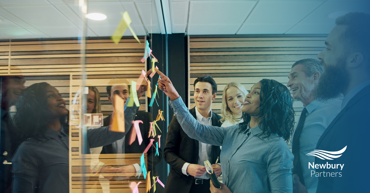 A group of professionals in an office examines a sticky note, utilizing visual task management for their hiring process.