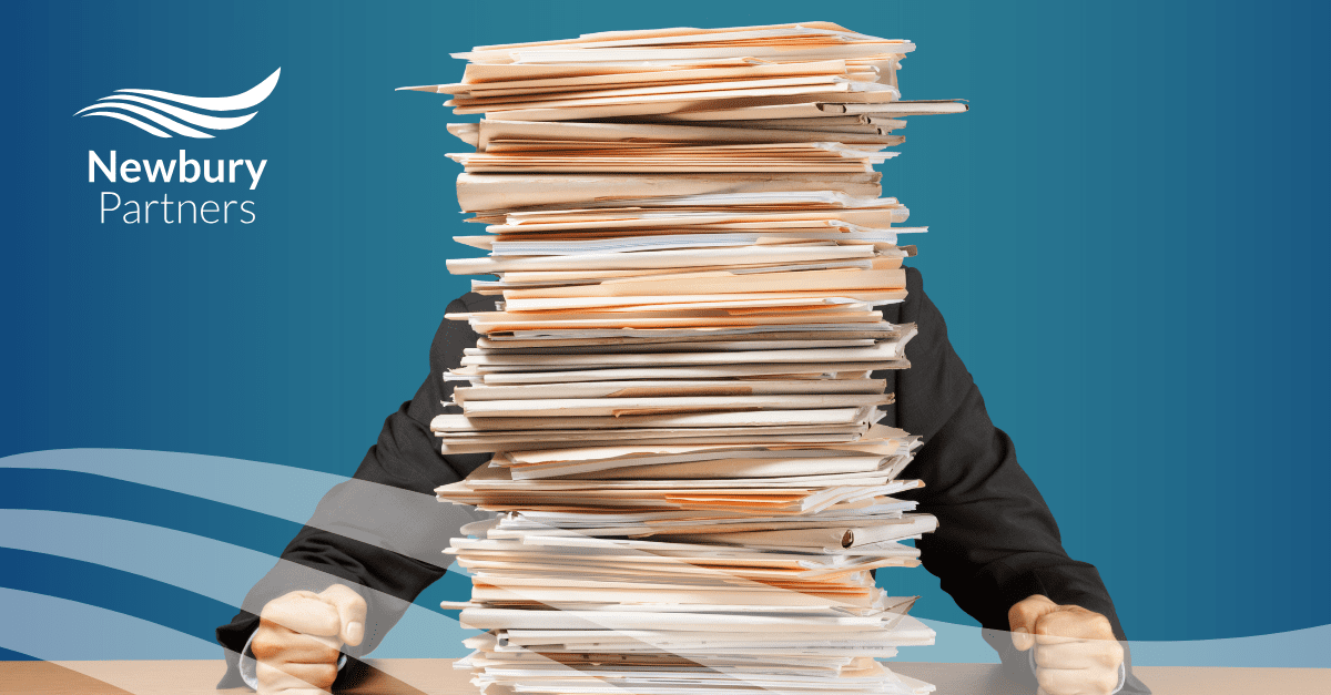 An overwhelmed professional sits behind a massive stack of paperwork, symbolizing the challenges of high-volume candidate screening and the need for automating recruitment processes.